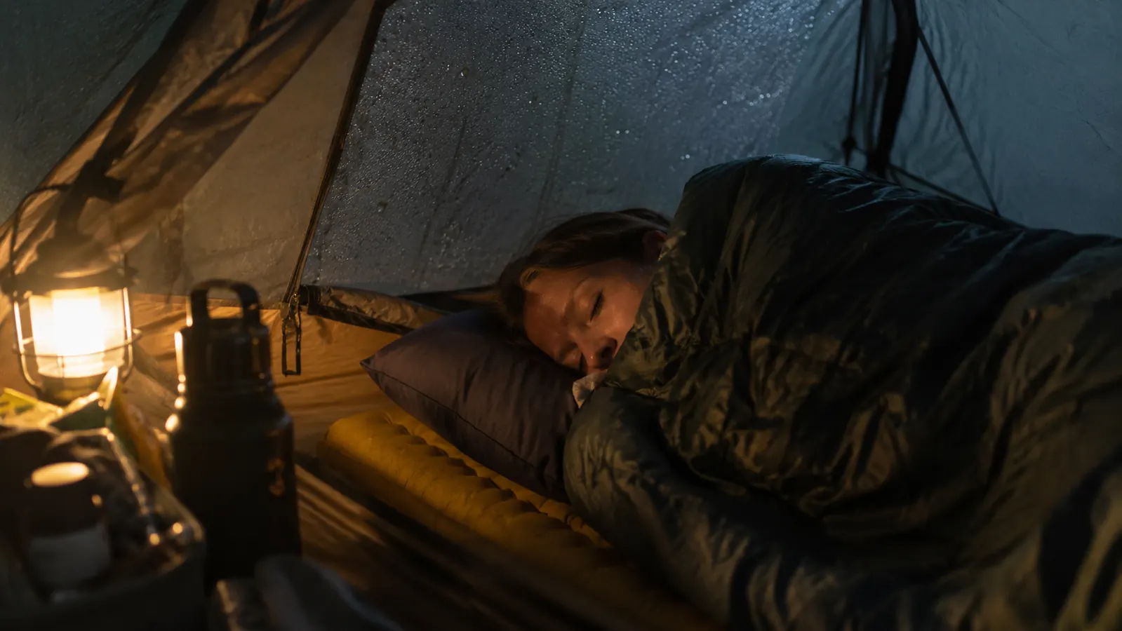 A camper sleeping in a tent on a cold morning, sleeping bag pulled up, condensation visible on tent walls