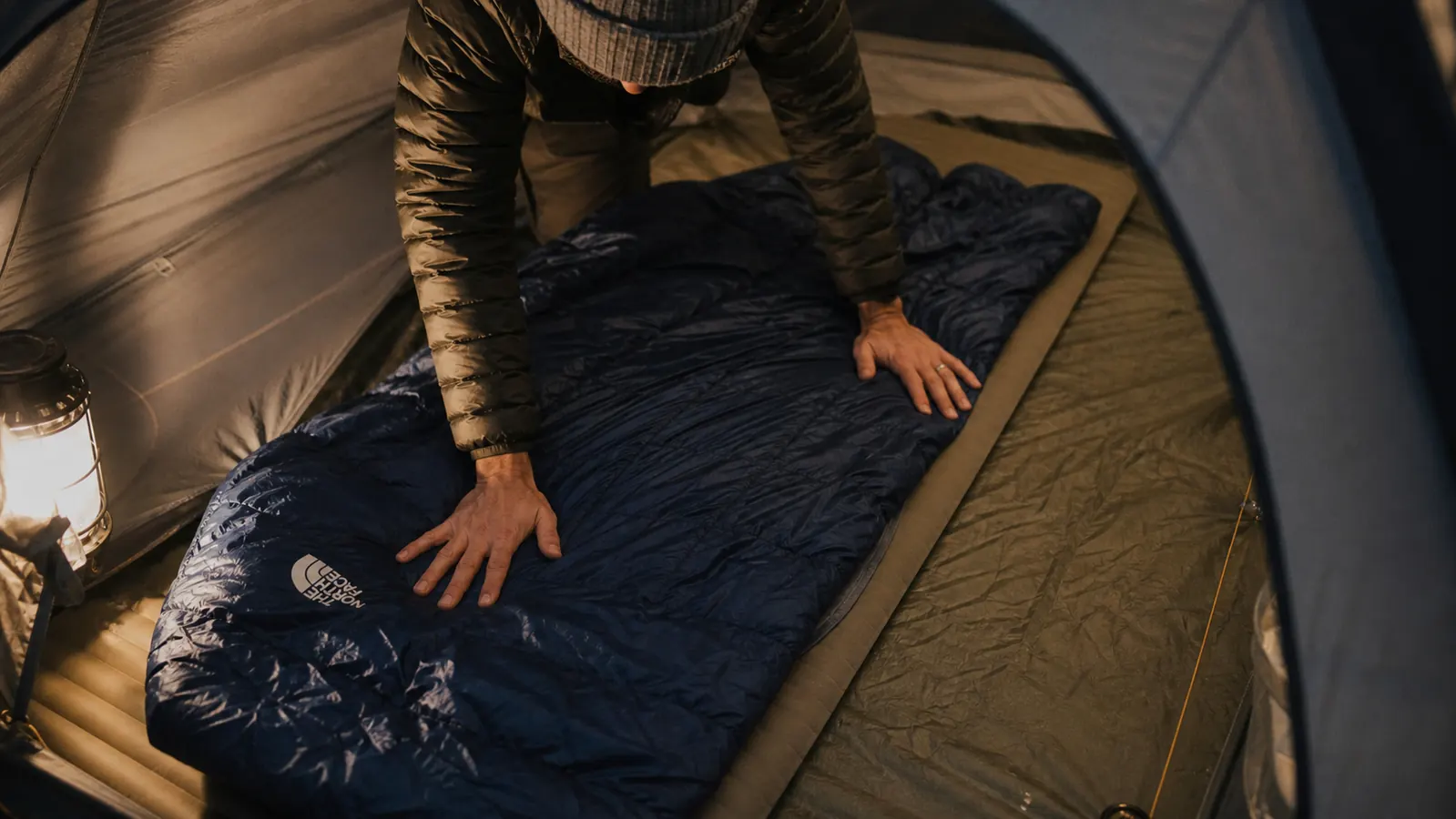 Camper laying out sleeping pad and sleeping bag inside tent at a forested campsite at night