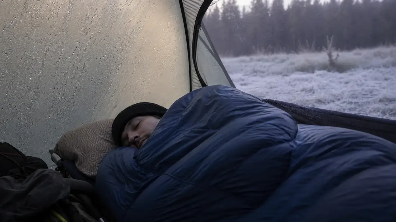 Camper sleeping comfortably inside a tent on a cold morning with frost visible outside